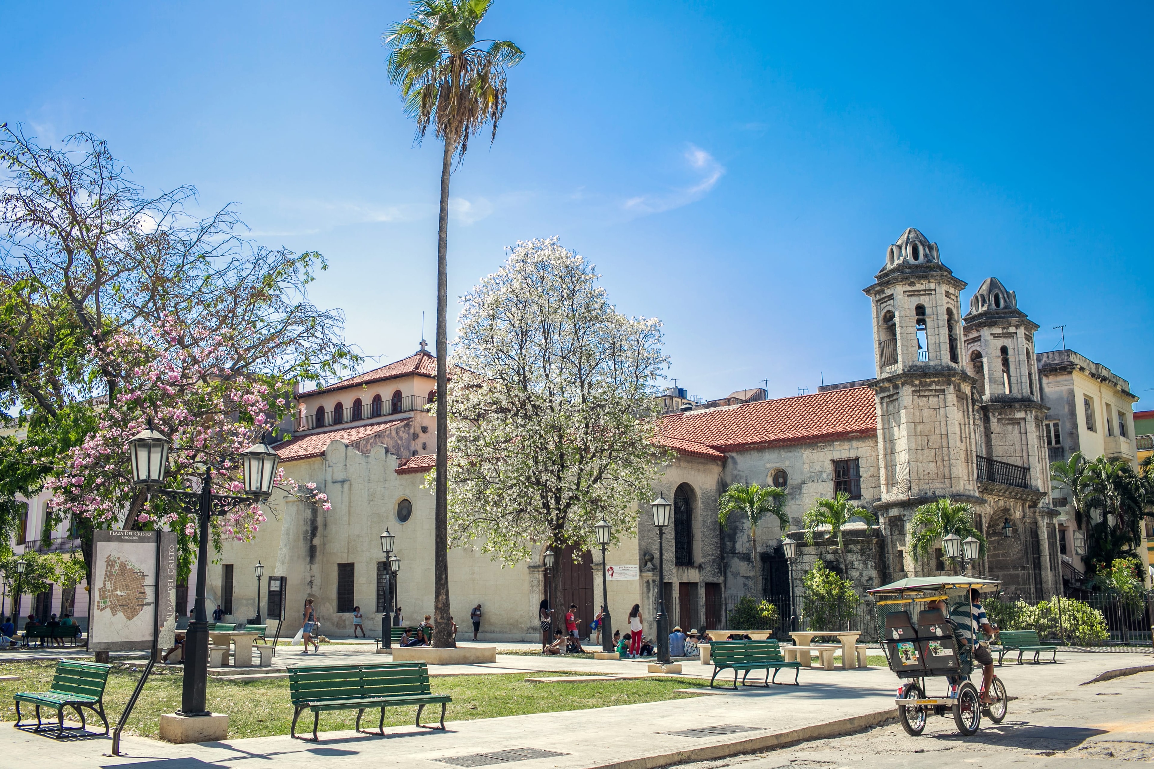 Plaza del Cristo Havana with stone church, flowering trees, park benches, and bicycle taxi, Cuba