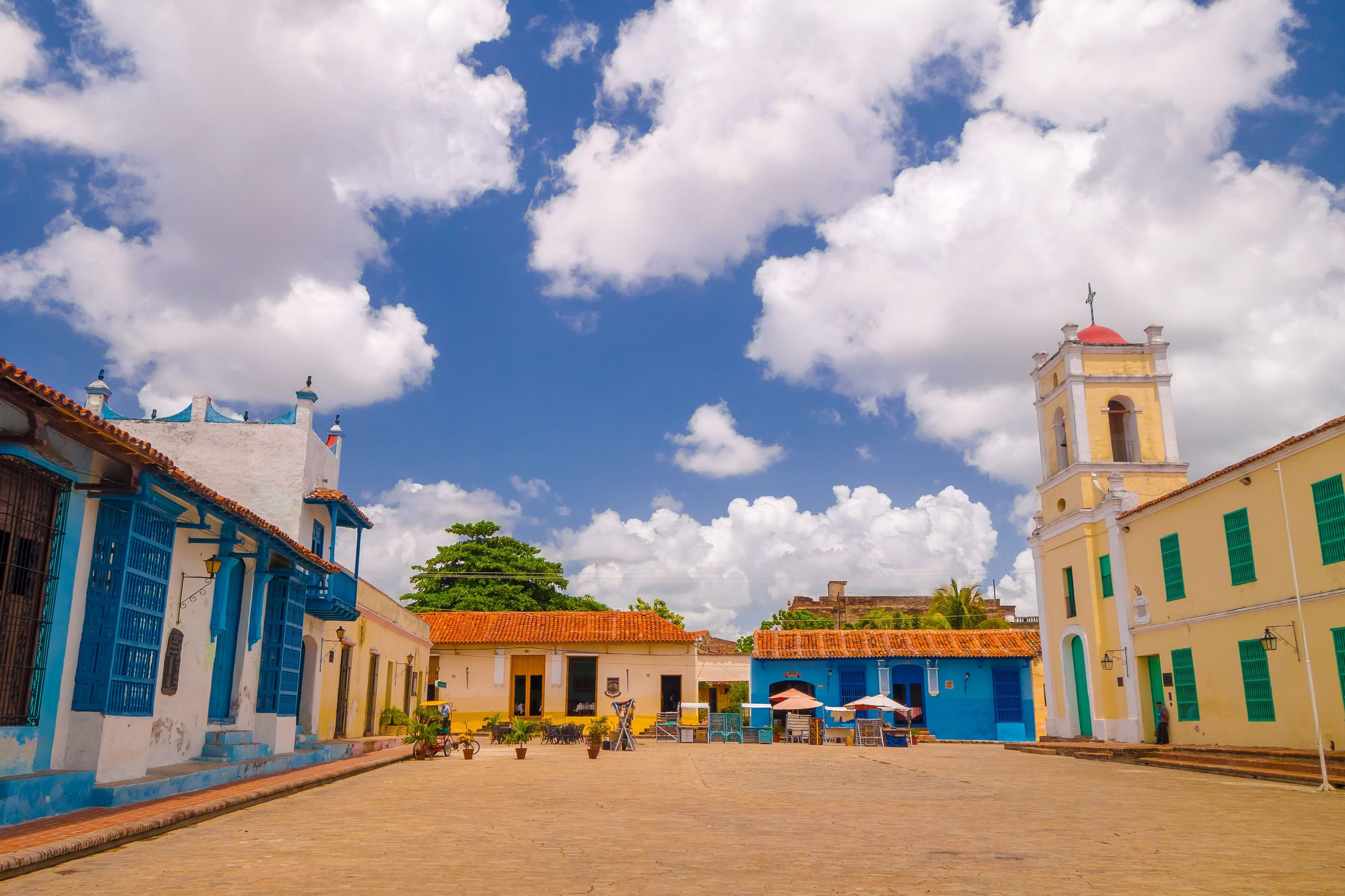Colorful colonial plaza in Camagüey with blue and yellow buildings, church bell tower, and bright sky, Cuba