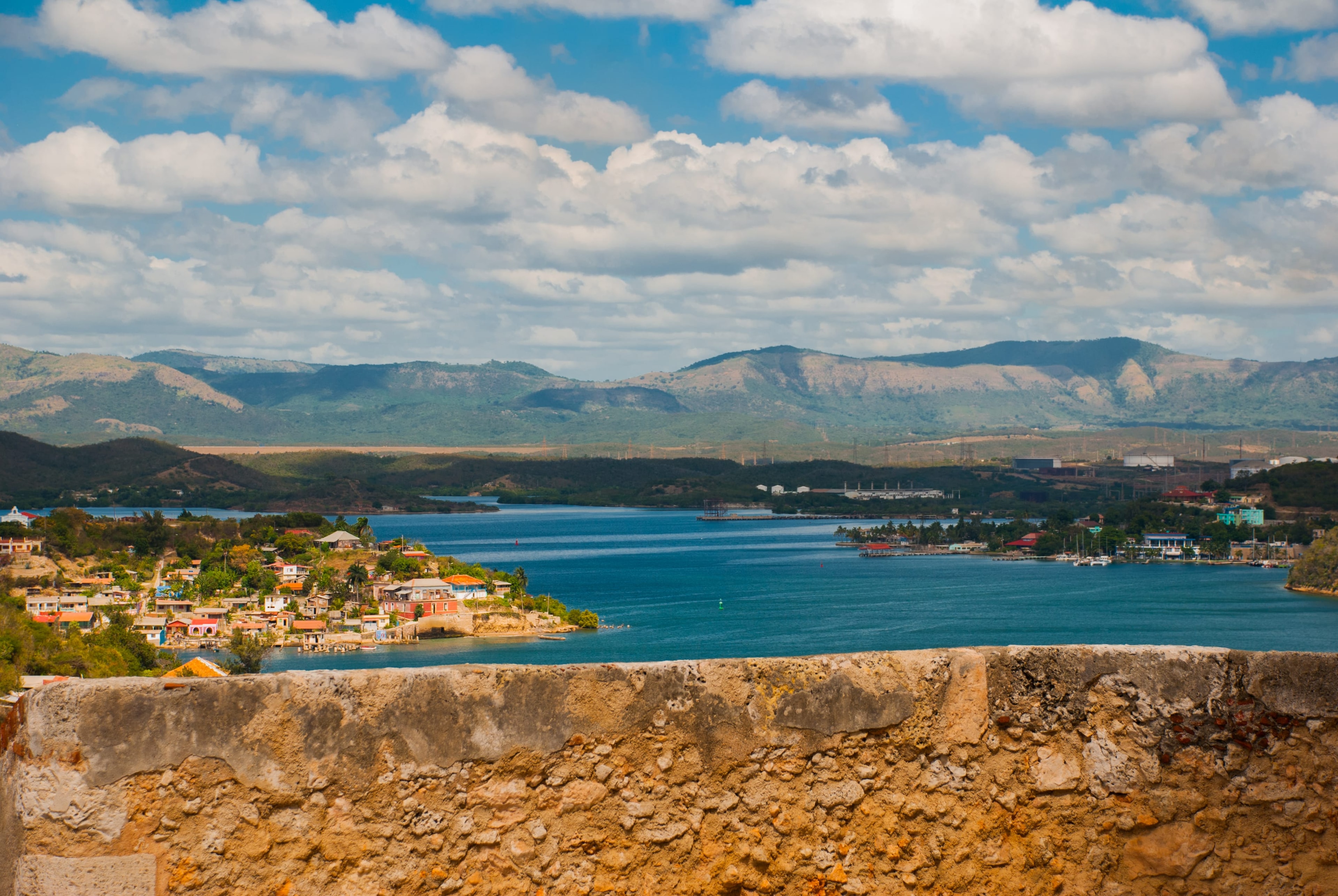 View from fortress wall over Cienfuegos bay with colorful waterfront village, marina, and green mountains, Cuba