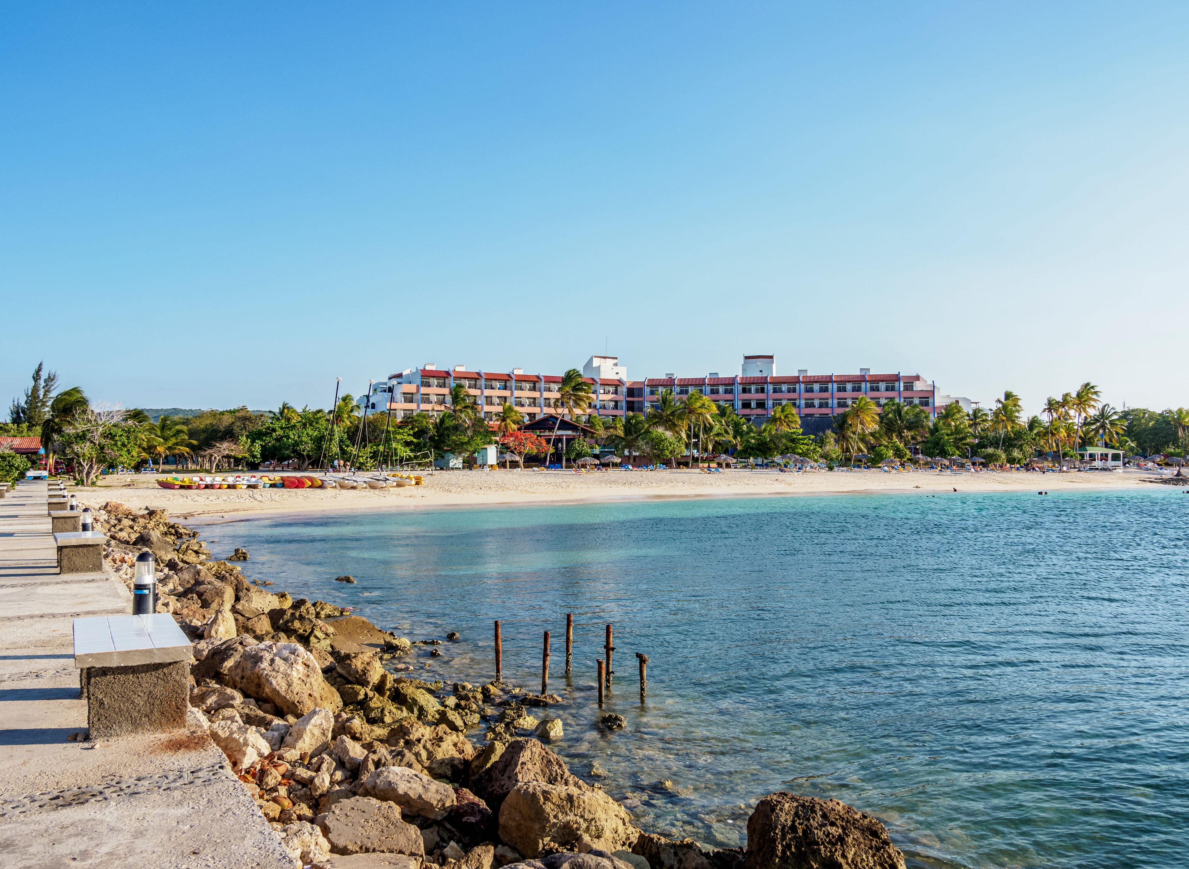 Cuba beach resort with sandy shore, turquoise water, palm trees, and hotel building under clear blue sky