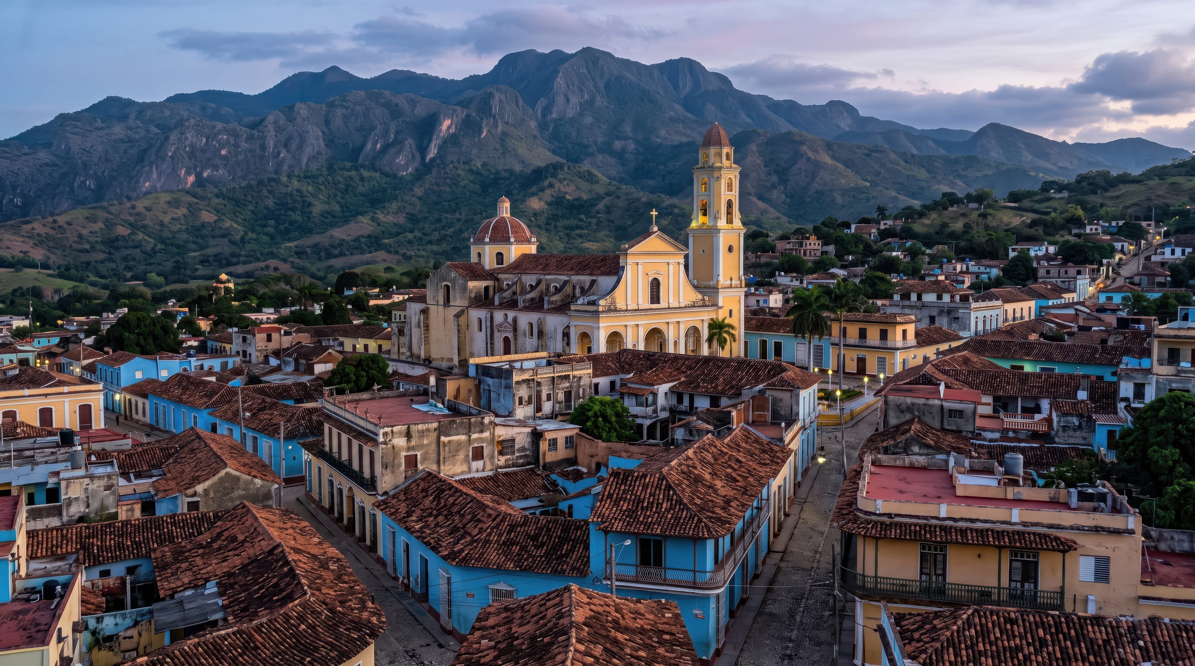 Aerial dusk view of Trinidad Cuba with yellow church, terracotta rooftops, and dramatic Escambray mountains, Cuba