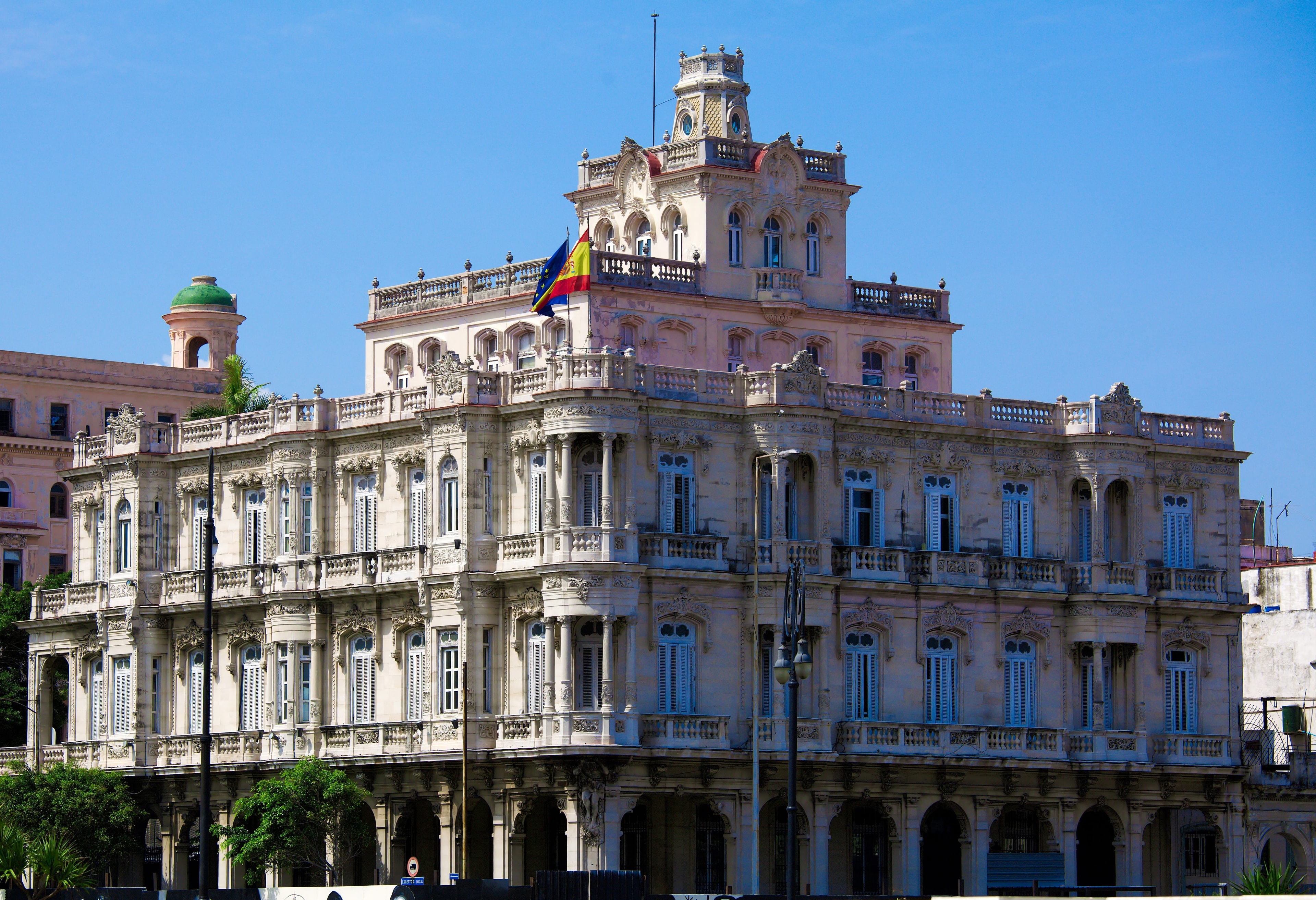 Ornate Spanish Embassy building with decorative tower, balustrades, and Spanish flag on Havana waterfront, Cuba