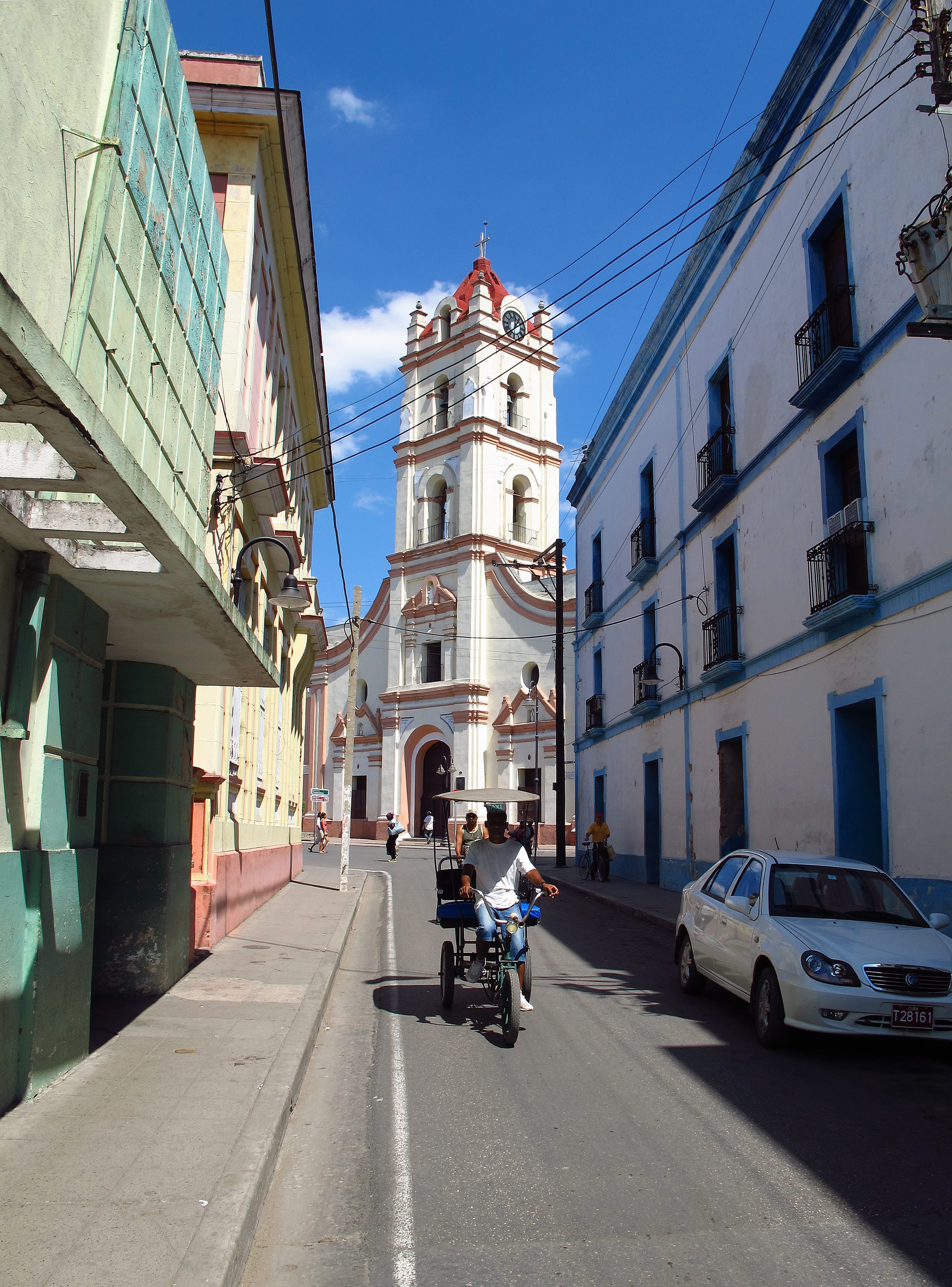 Camagüey street scene with white and red-trimmed church bell tower and bicycle taxi heading toward the cathedral, Cuba