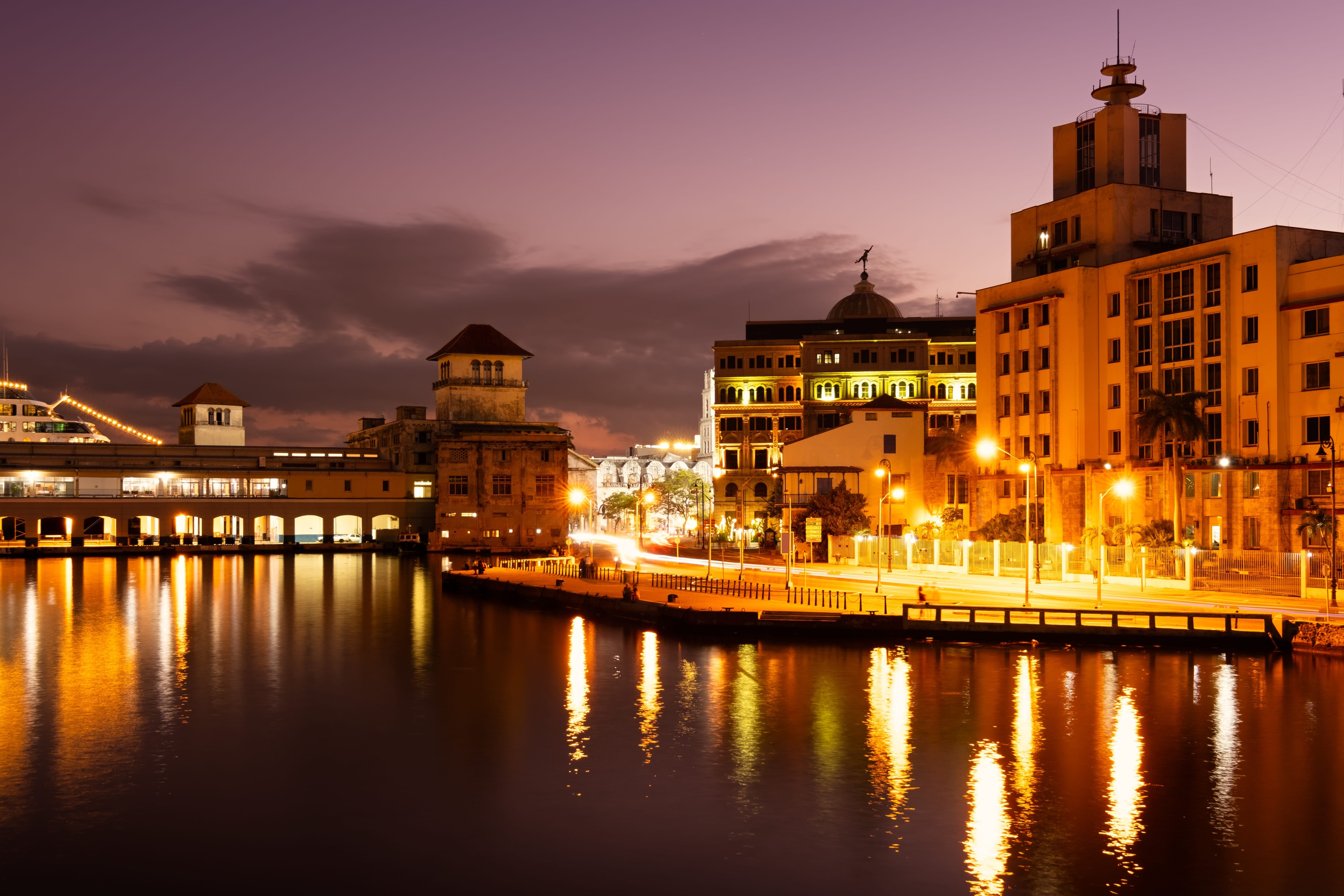 Havana harbor at night with golden reflections on still water, illuminated port buildings, and church dome silhouette, Cuba