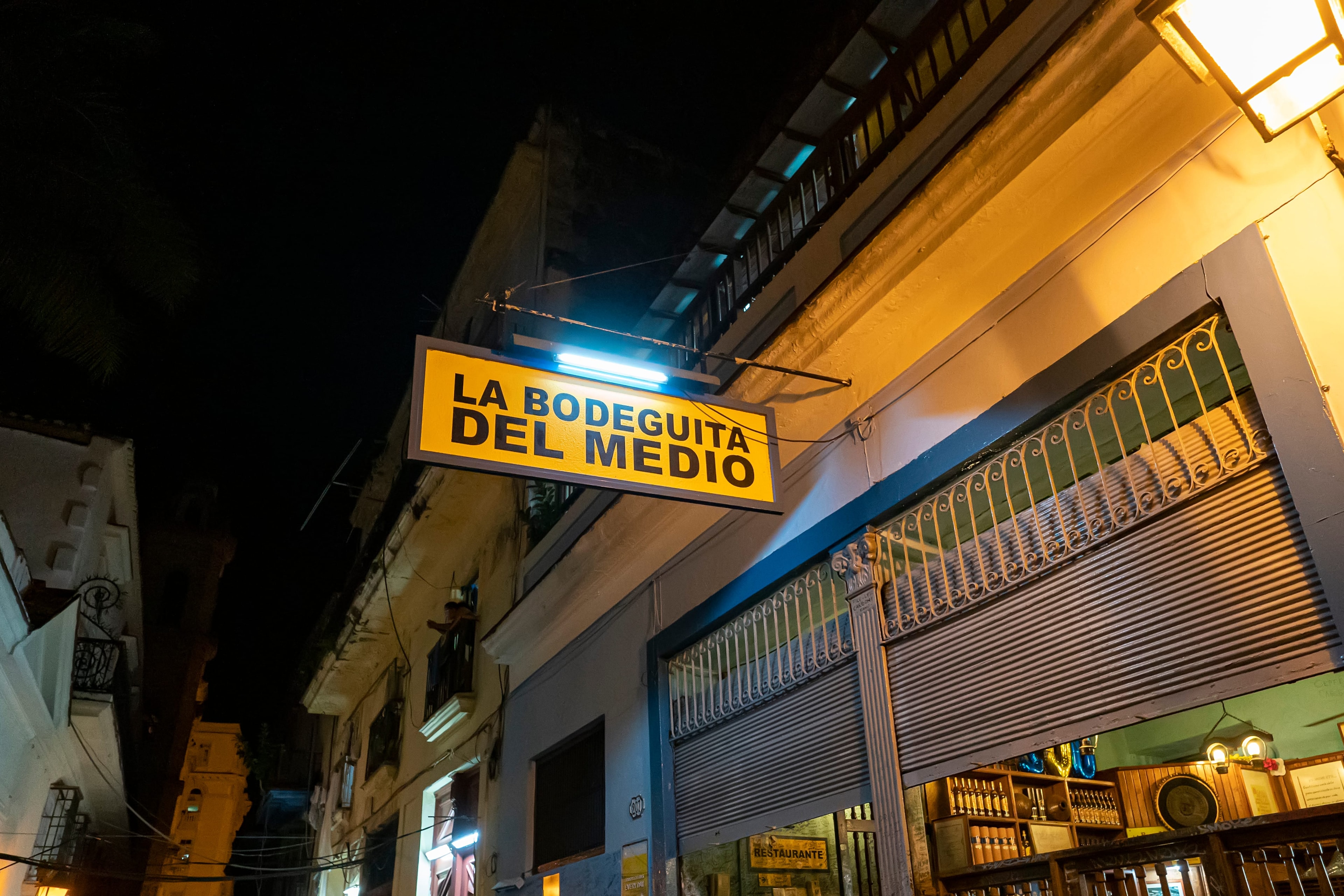 La Bodeguita del Medio iconic yellow sign lit up at night on a narrow Old Havana street, Cuba