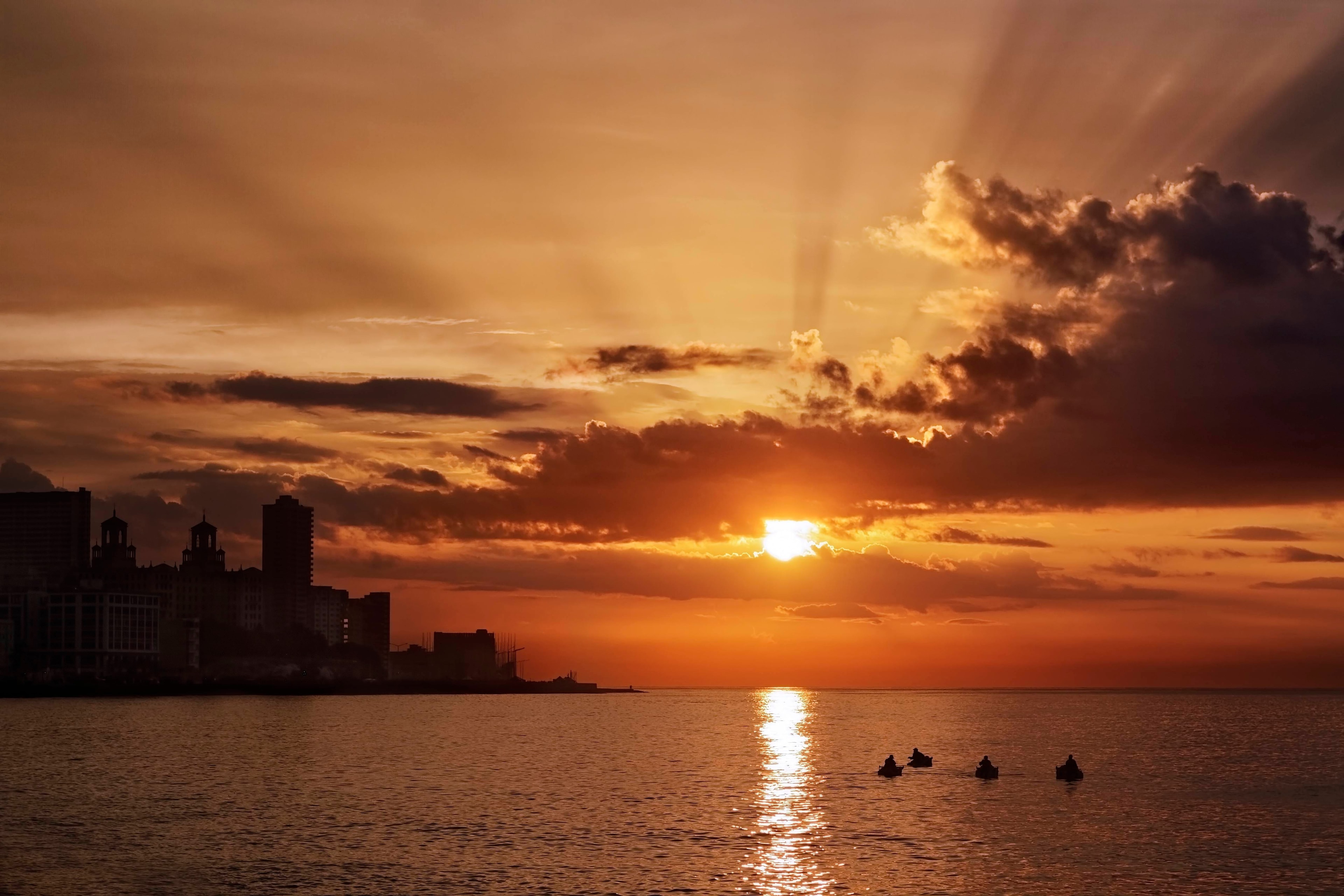 Fiery orange and gold sunset over Havana bay with silhouetted skyline, dramatic clouds, and fishermen on the water, Cuba
