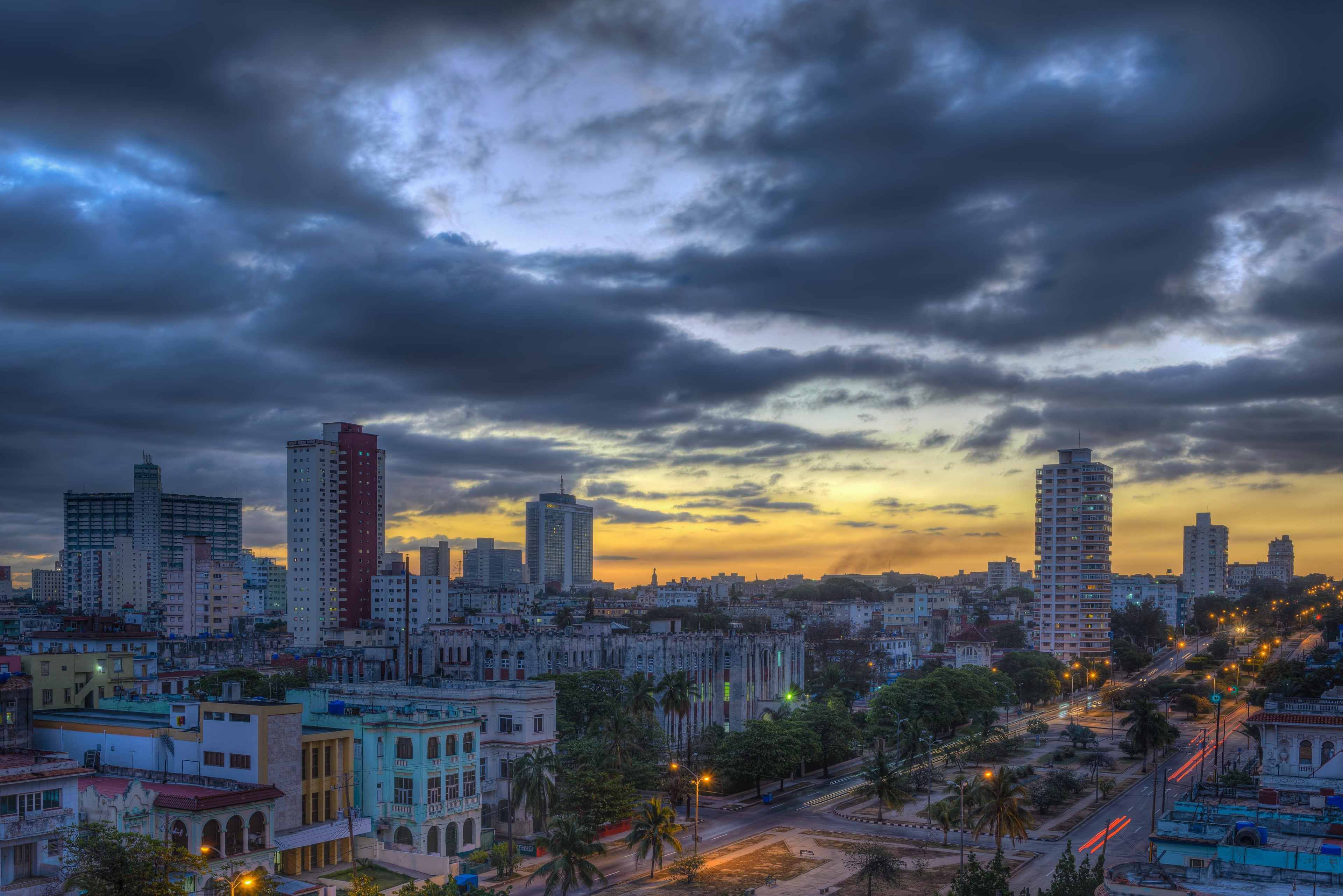 Havana skyline at dusk with El Capitolio dome, modern towers, and city lights glowing under a vivid orange and purple sky, Cuba