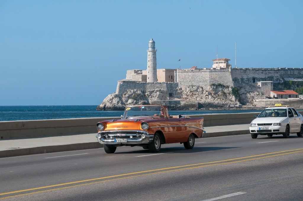 Vintage orange convertible on Malecón with Castillo del Morro Cuba