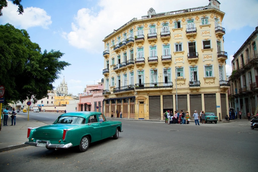 Teal vintage car on Havana street corner with yellow colonial building and balconies