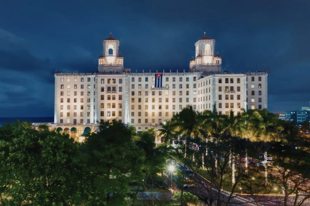 Hotel Nacional de Cuba illuminated at night with Cuban flag and palm trees