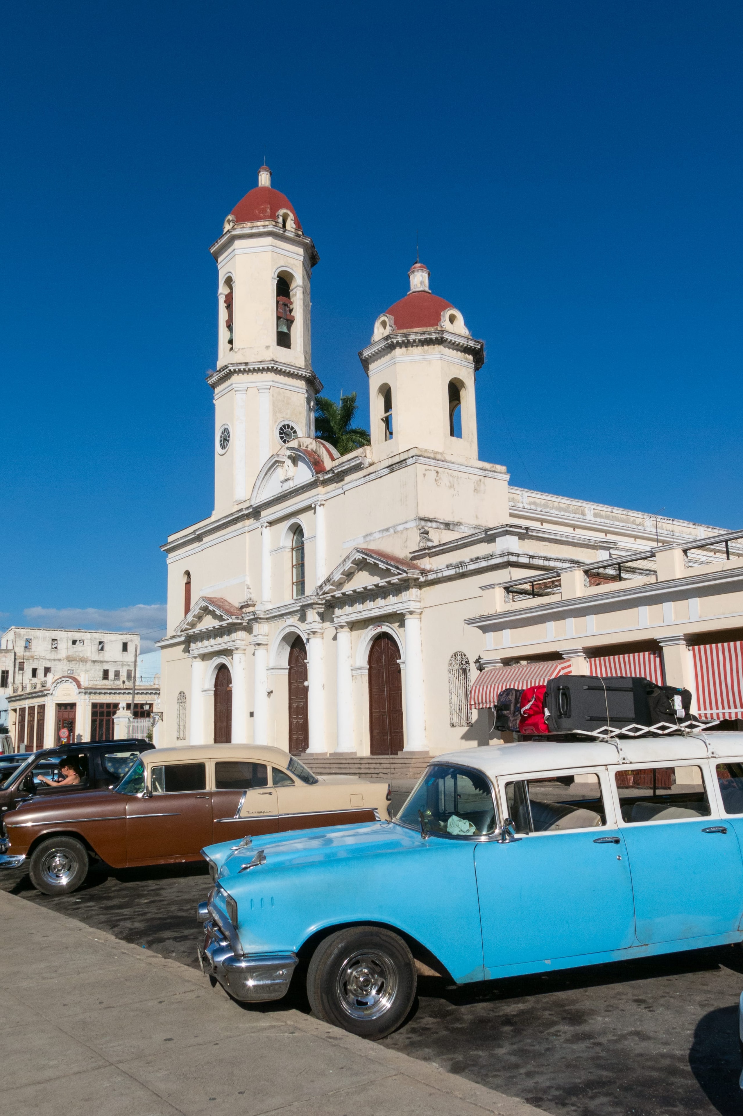 Vintage blue and brown classic cars parked outside Cienfuegos Cathedral Cuba