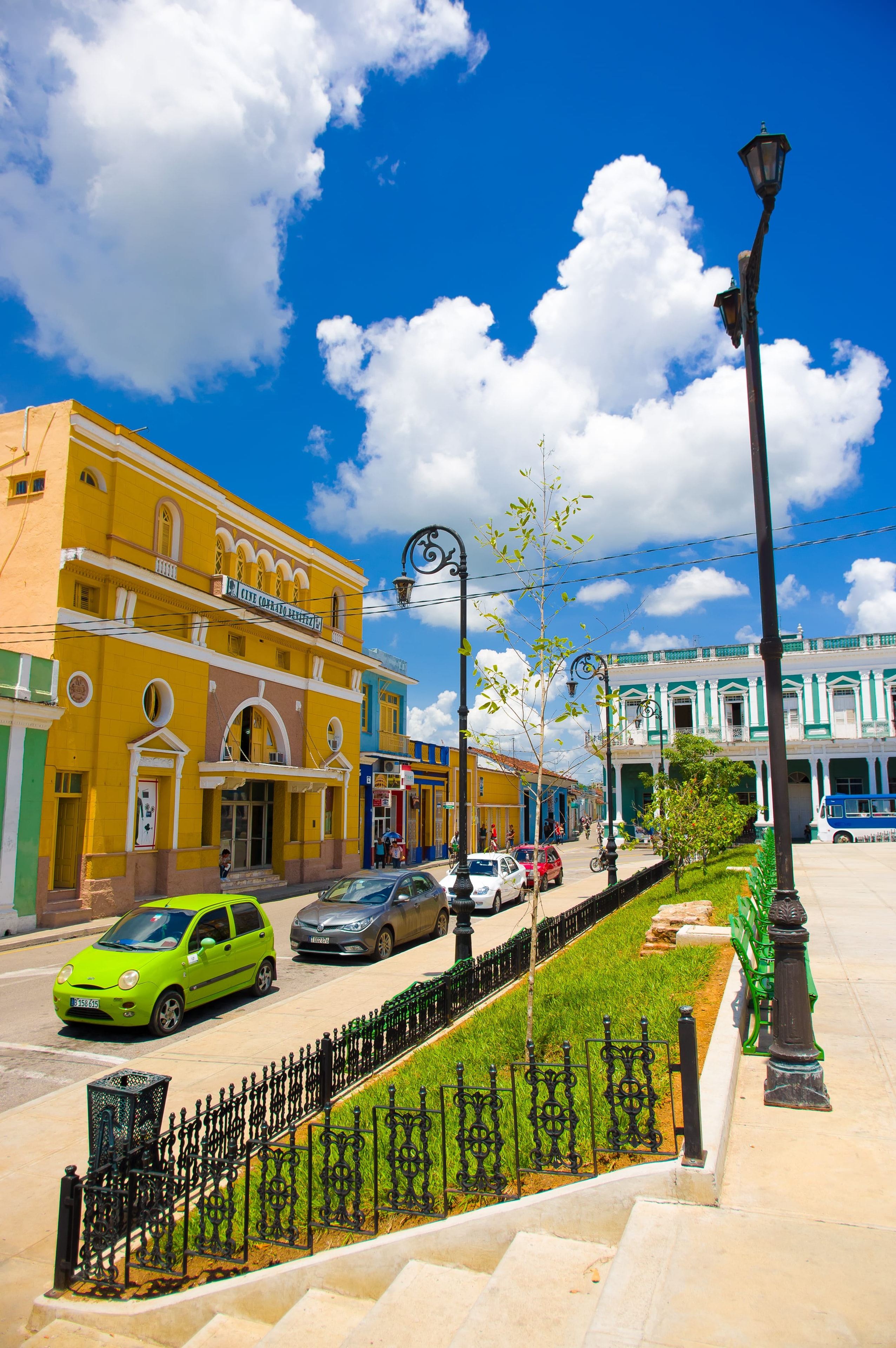 Vibrant colonial street scene with yellow cinema building and ornate iron lampposts, Cuba