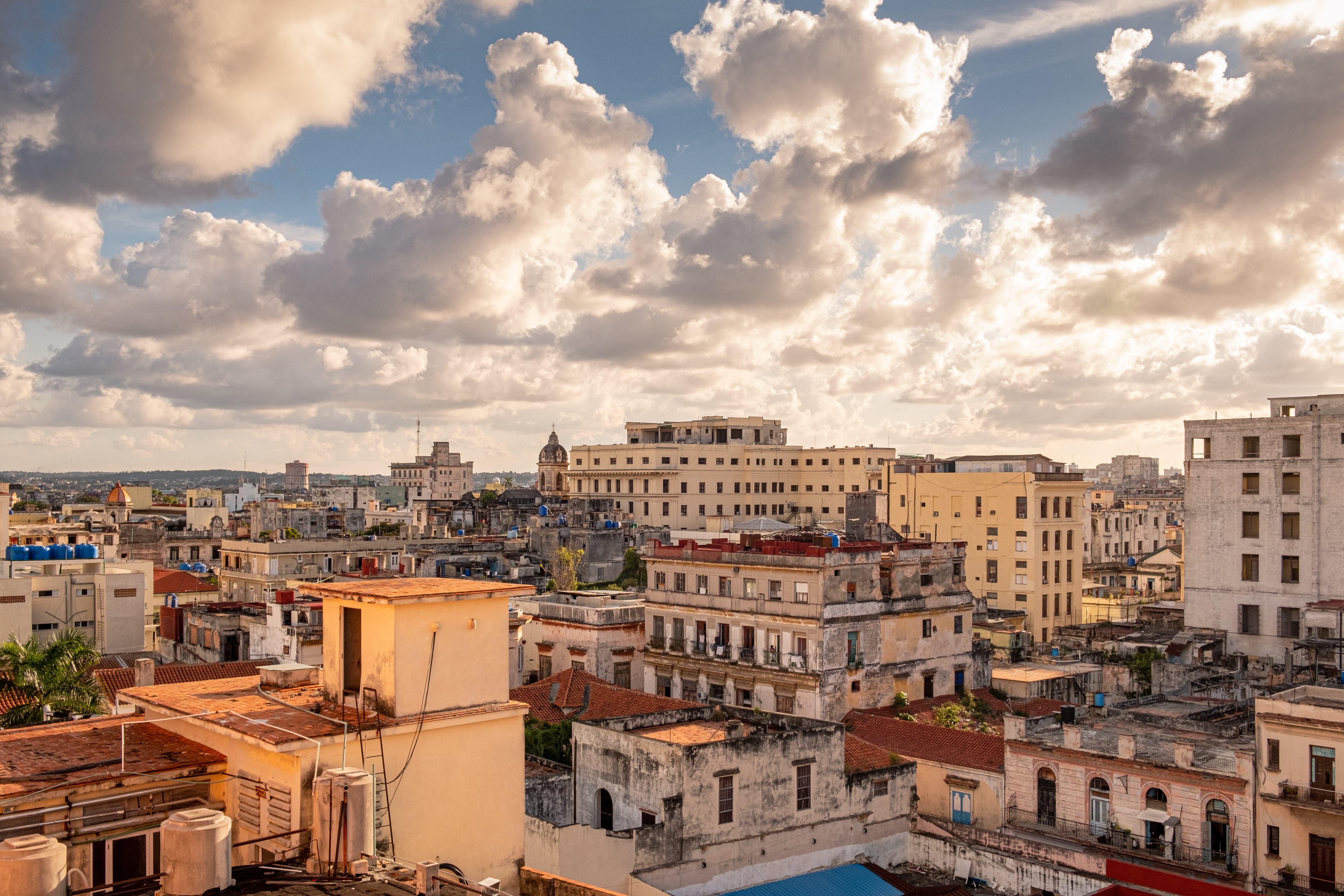 Havana rooftop panorama with colonial buildings, red-tiled roofs, and dramatic cloudscape at golden hour, Cuba